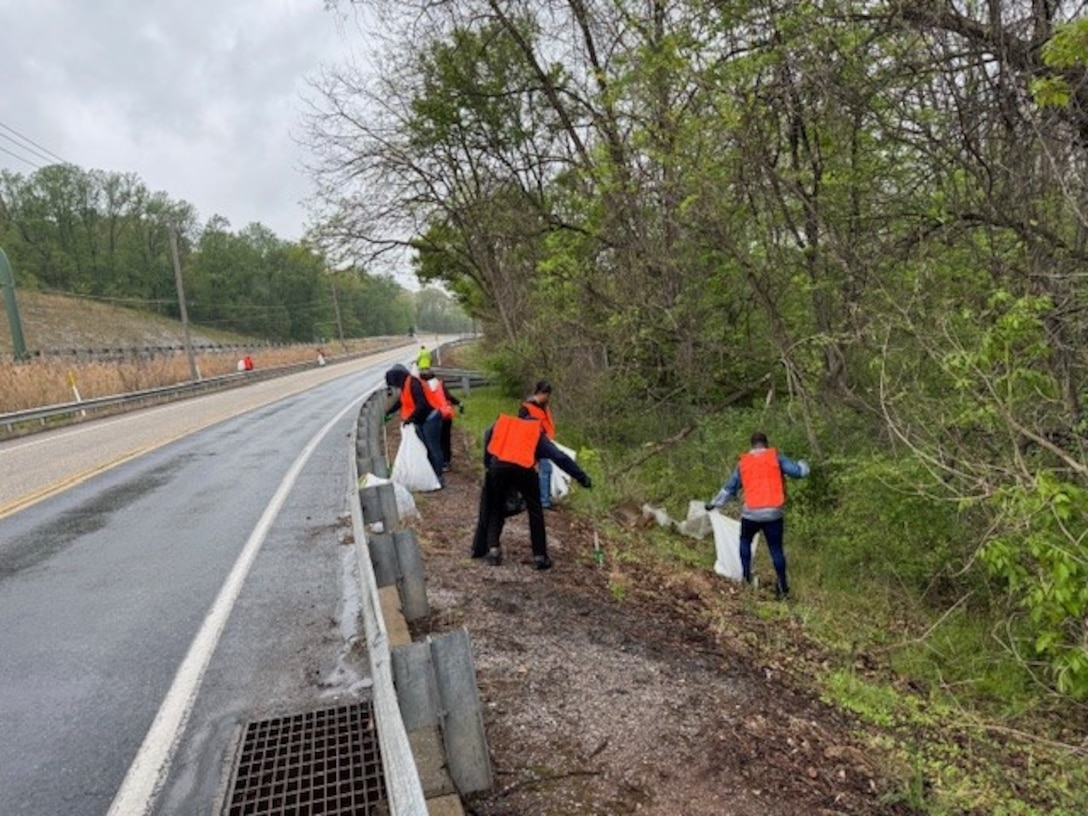 A group of people in reflective safety vests pick up trash alongside a road.