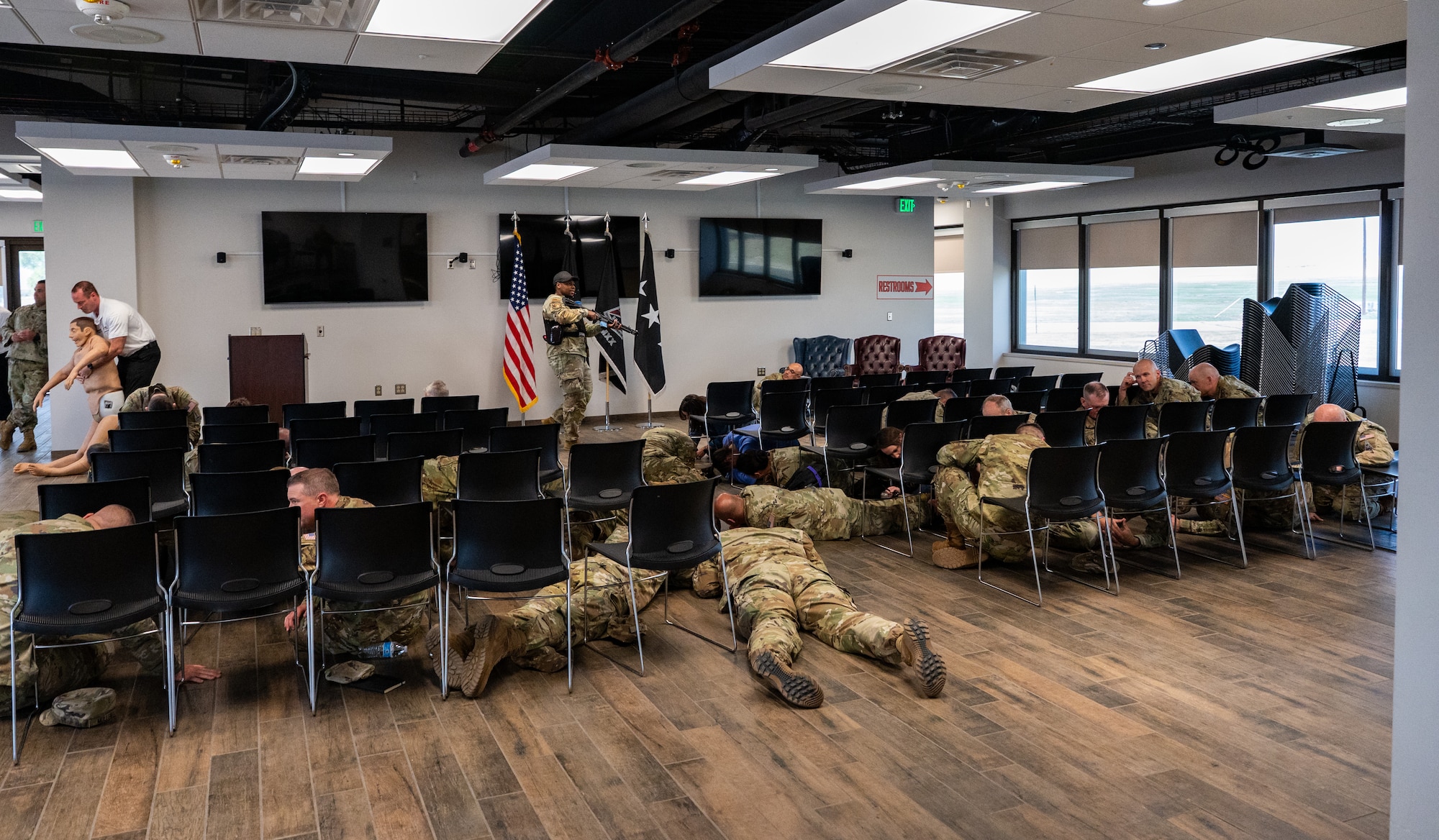 Military members take cover on ground and behind chairs during an active shooter exercise.