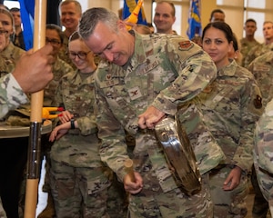 An Airman in OCPs bangs on a bedpan like a drum with a stick.