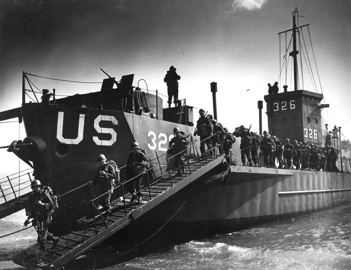 Troops disembark from a landing craft with their weapons and gear.