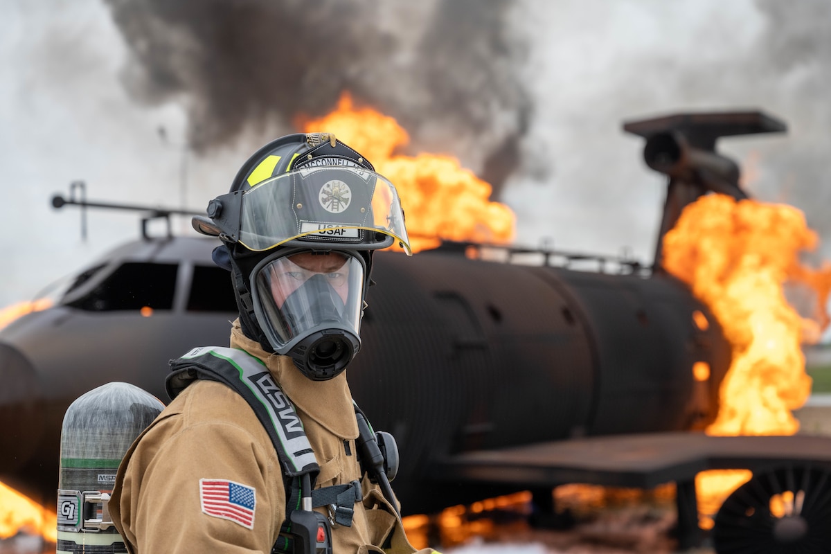 Airman 1st Class Garrett Smith, 22nd Civil Engineer Squadron firefighter, stands in front of a simulated burning aircraft during Exercise Lethal Stack at McConnell Air Force Base, Kansas, May 6, 2025. Lethal Stack puts McConnell’s survivability, connectivity and agility to the test, enhancing its ability to rapidly deploy and continue operating in degraded environments. (U.S. Air Force photo by Airman 1st Class Patrick O’Neill)