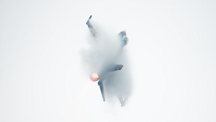 an F-16 fighter jet flies through the sky in a hard turn, causing pressure vapors to engulf most of the aircraft