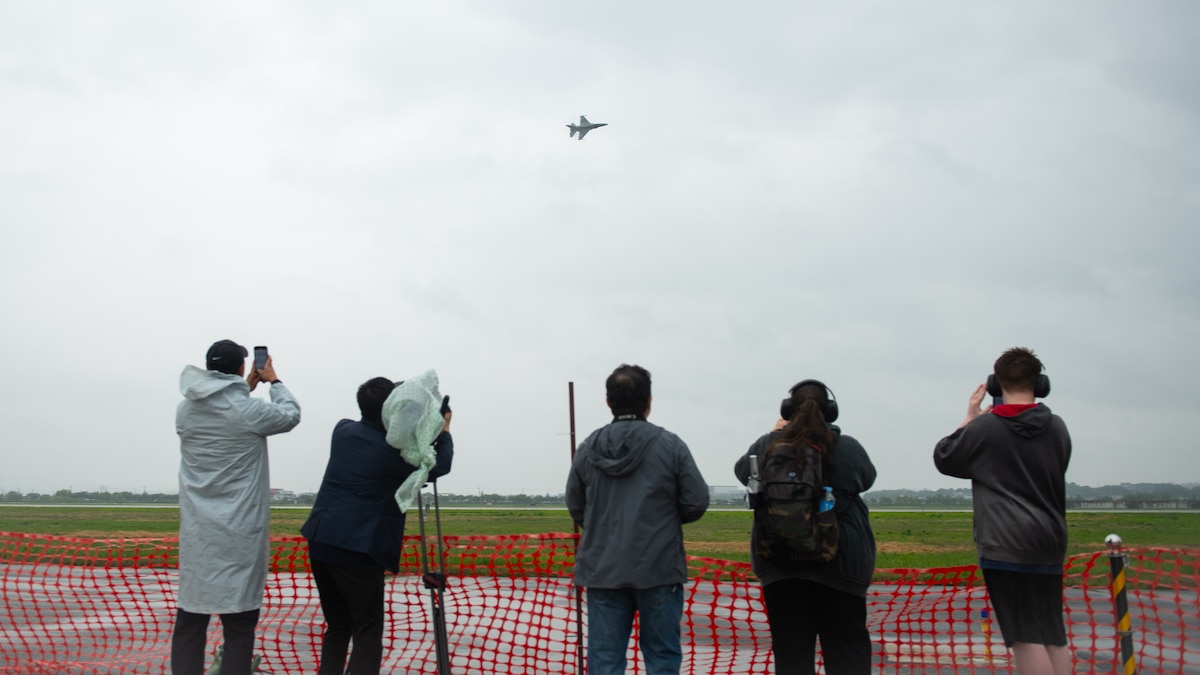 people take photos and video of a fighter jet flying across the sky