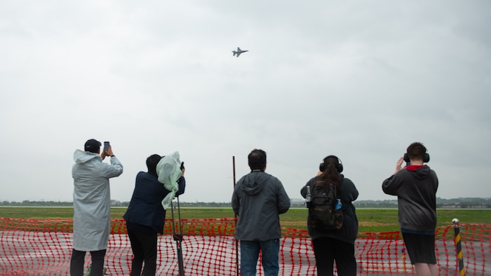people take photos and video of a fighter jet flying across the sky