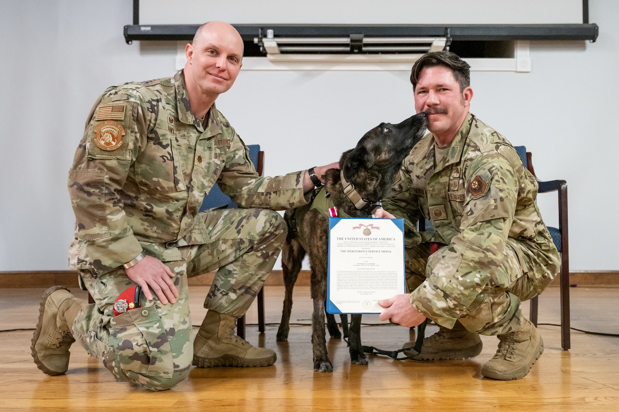 Master Sgt. Rudy Parsons, right, a pararescueman assigned to the 123rd Special Tactics Squadron, accepts a Meritorious Service Medal from unit commander Maj. Bryan Hunt, left, on behalf of Callie, center, the only certified search-and-rescue dog in the Department of Defense, during Callie’s retirement ceremony at the Kentucky Air National Guard Base in Louisville, Ky., Jan. 24, 2025. Over the course of more than six years with the unit, Callie served on numerous exercises and six real-world deployments, searching for survivors in the aftermath of floods, tornadoes, a mine collapse and an avalanche. (U.S. Air National Guard photo by Dale Greer)