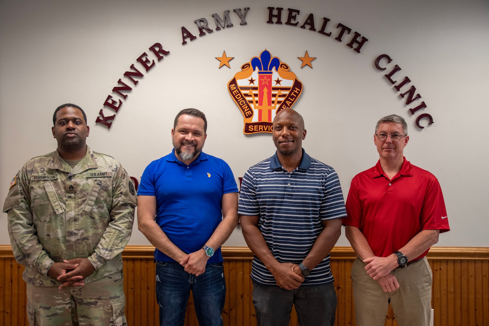 Four men posing in front of the Kenner AHC logo, celebrating Healthcare Technology Management week
