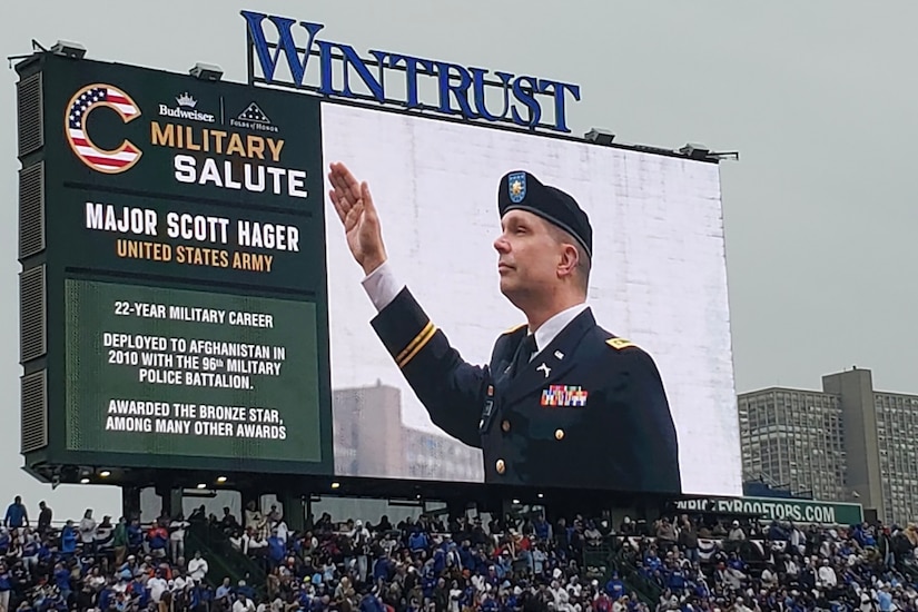 Maj. Scott D. Hager, 85th U.S. Army Reserve Support Command, waves to cheering baseball fans, on the jumbotron, during the Military Salute at the Chicago Cubs Hometown Opener game versus the San Diego Padres on April 4, 2025, at Wrigley Field.
