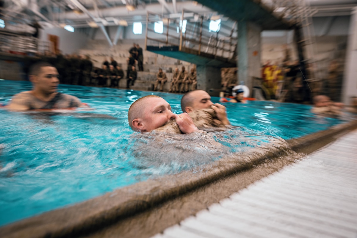 Marine recruits up to their neck in pool water use a uniform as a flotation device.