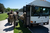 Airmen board a white bus outside on a sunny day.