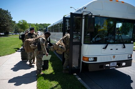 Airmen board a white bus outside on a sunny day.