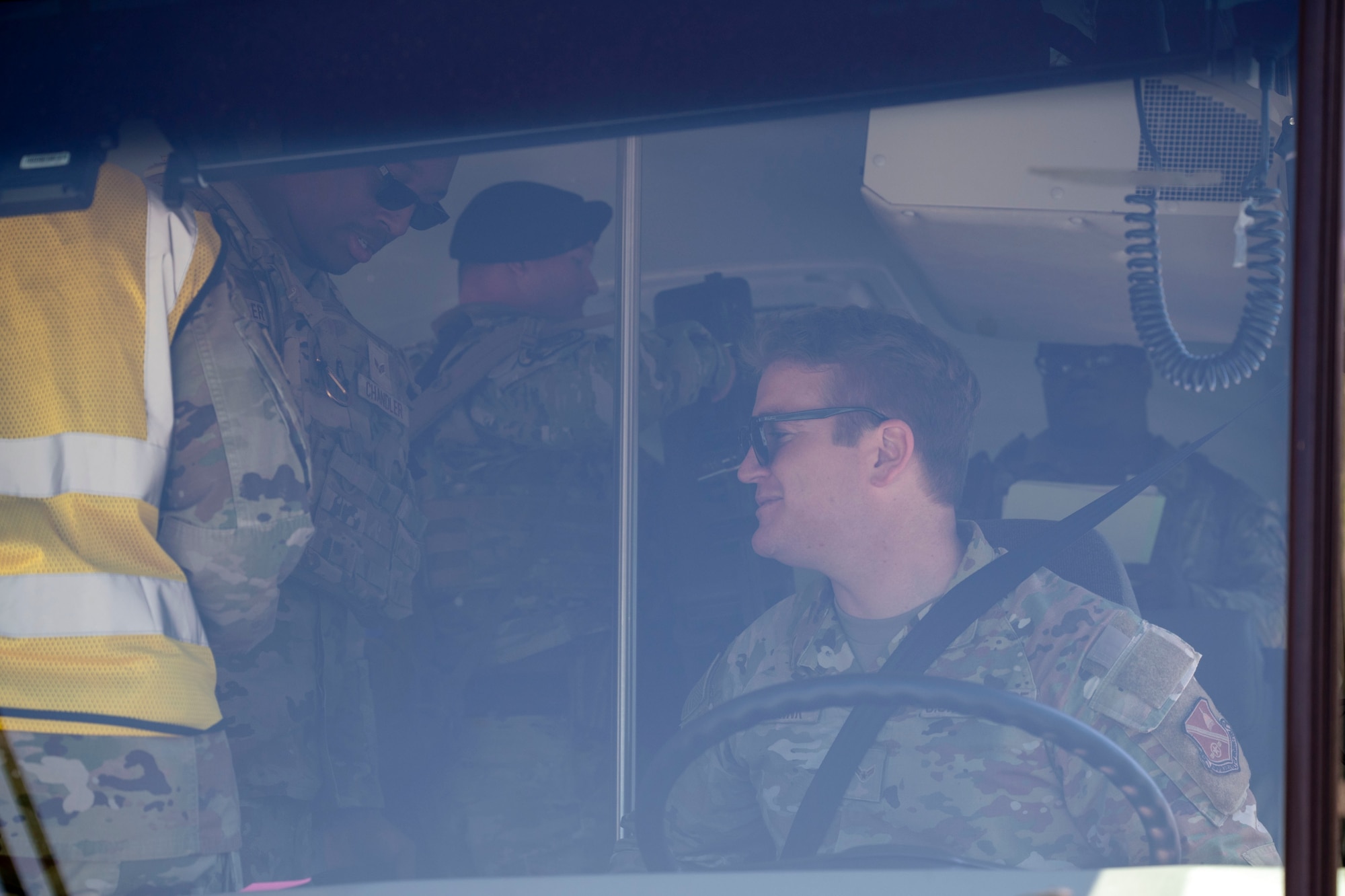 Airman sits behind a bus steering wheel and turns to his right to greet passengers.