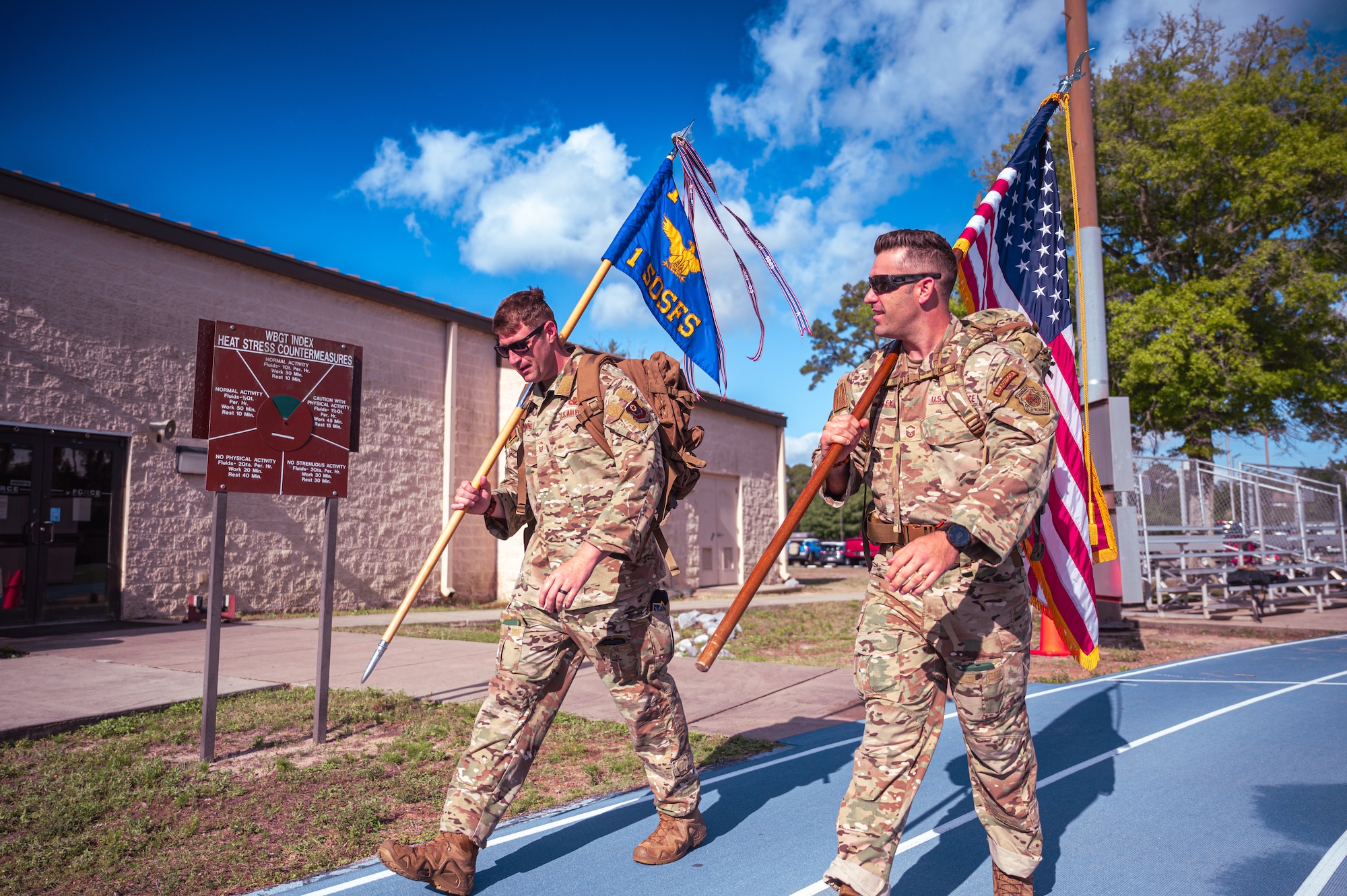 Two defenders carry a U.S. Flag and a Security Forces guidon on the track to begin the Vigilance Ruck.