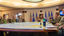 Eight people in uniform sit around a large, square table with a map covering the surface.