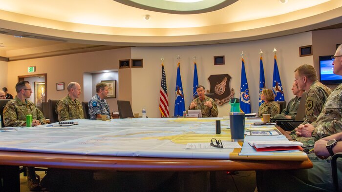 Eight people in uniform sit around a large, square table with a map covering the surface.