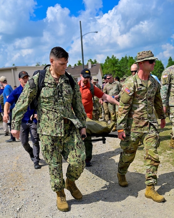 250404-N-BC658-1935 FORT BRAGG, NC (Apr. 04, 2025) Master Chief Corpsman Charles Hickey, command master chief of the Navy Medicine Operational Training Command (NMOTC)(left), carries a stretcher with a simulated patient to assist special operations medical personnel comprised of Soldiers and Sailors of the U.S. Army John F. Kennedy Special Warfare Center and School's; Joint Special Operations Medical Training Center (JSOMTC) during a mass casualty event demonstration during the CAPEX2025 exercise on Fort Bragg, North Carolina, April 4, 2025. JSOMTC provides world-class medical and skills training to special operations medical personnel of the Army, Navy and Marine Corps. (U.S. Navy photo by Mass Communication Specialist 1st Class Russell Lindsey SW/AW)