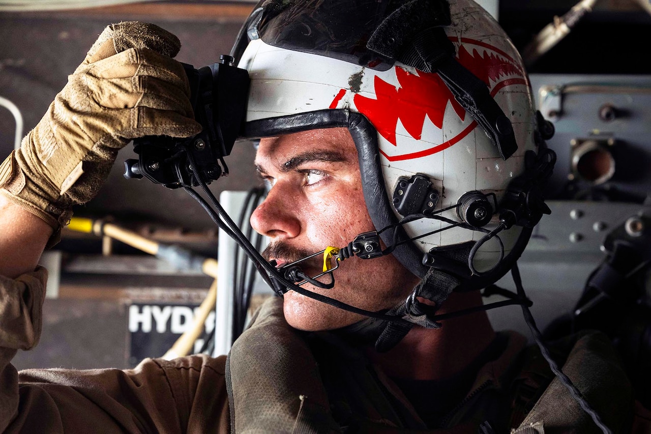 A close-up of a Marine as they adjust their helmet in an aircraft.