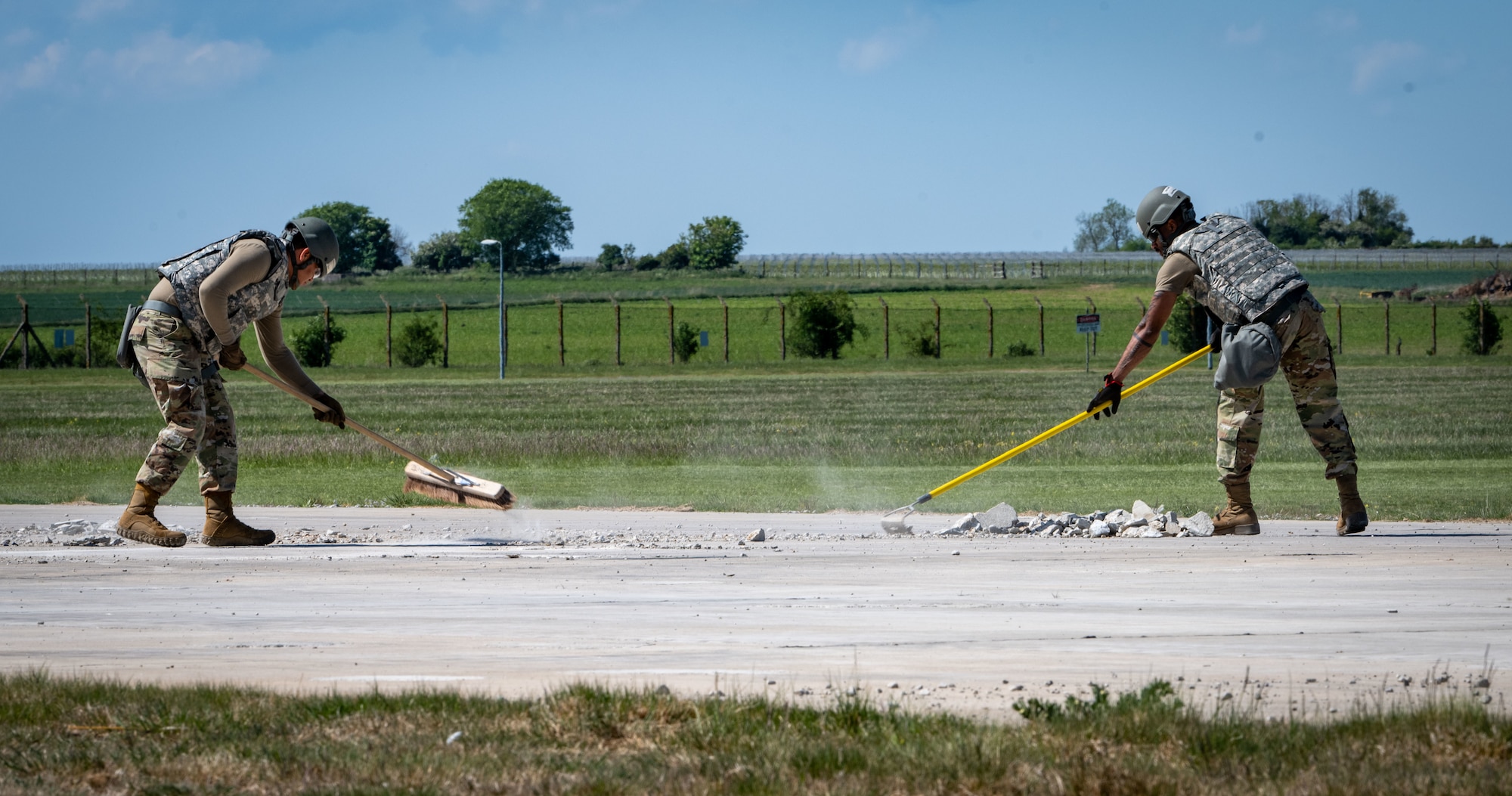 U.S. Airmen assigned to the 100th Civil Engineer Squadron use brooms to brush away debris while repairing damage to the runway during combat readiness inspection Skyway Chariot at RAF Feltwell, England, May 9, 2025.
