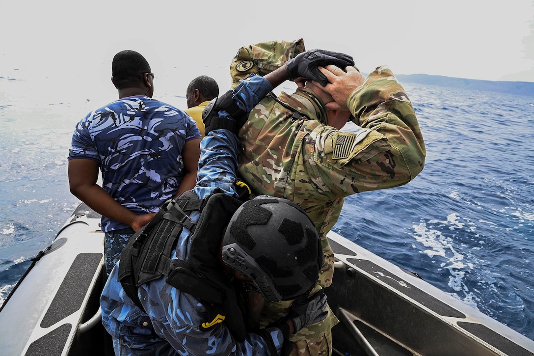 U.S. and Djiboutian sailors stands on a partially visible boat as it transits a body of water.