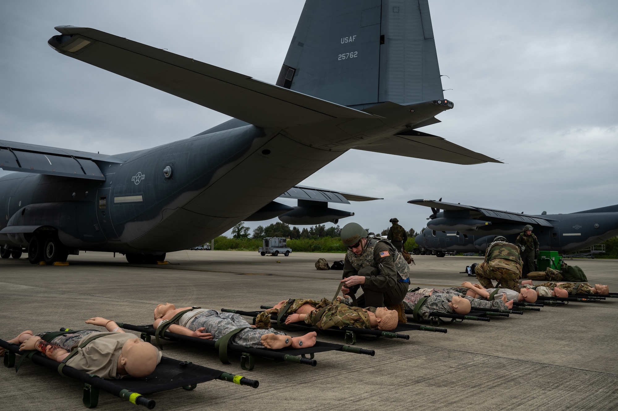Military medical Airmen kneel over simulated patients on stretchers lined up to be loaded outside of a MC130-J