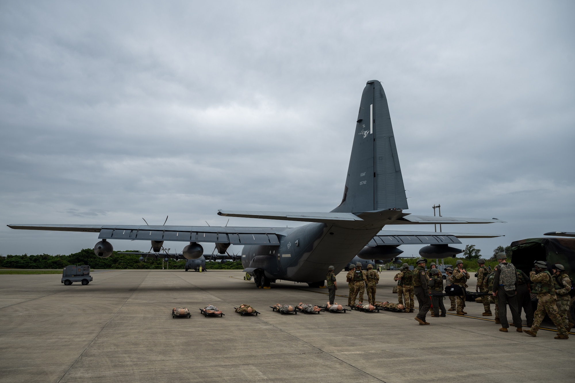 Military medical Airmen stand outside of a MC130-J with simulated patients on stretchers lined up to be loaded into the aircraft