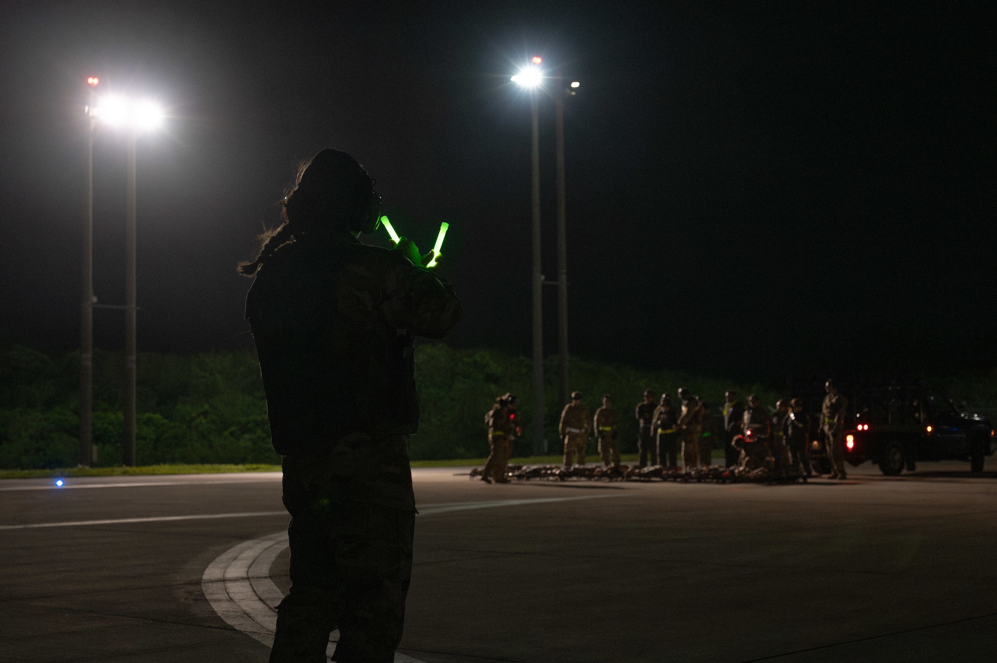 A military member ushers other Airmen to load cargo on a flight line at night
