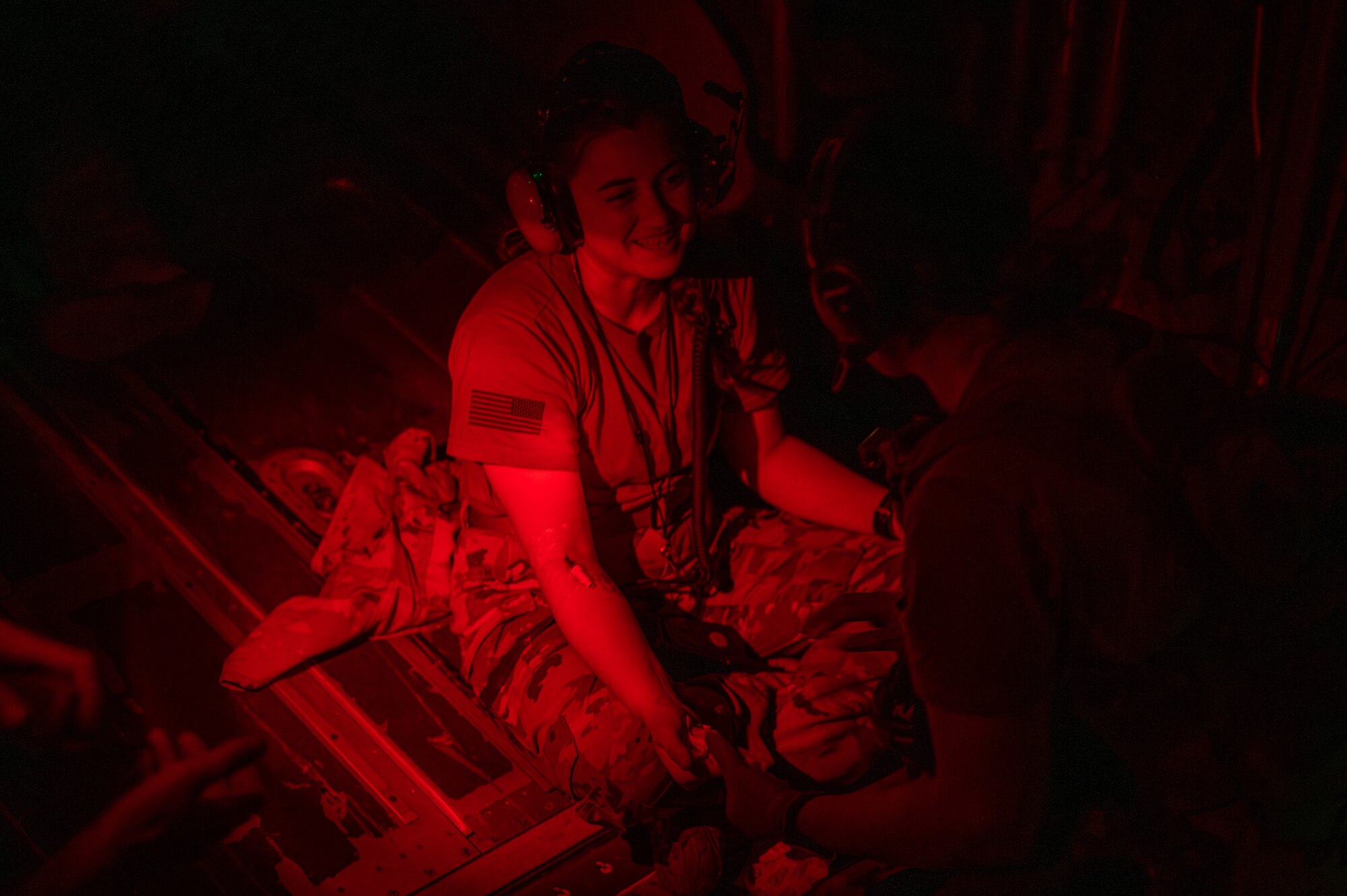 A military member sits on the floor of a aircraft after being given a IV under red light low light