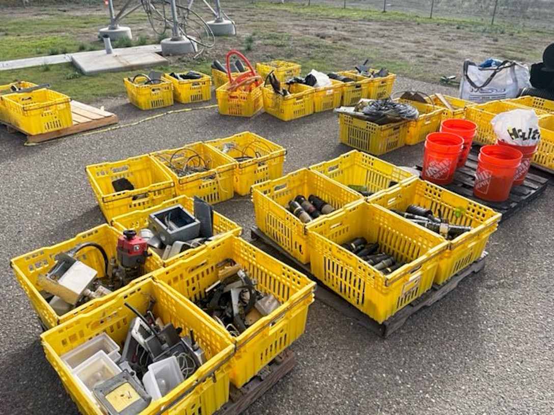 More than a dozen yellow bins on pavement contain parts
