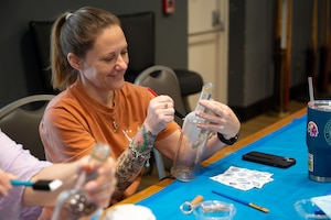 Amanda Hendrick, 17th Integrated Resilience Office prevention specialist, paints a bottle with adhesive during the Spouse Resiliency & Wellness Day at the Powell Event Center, Goodfellow Air Force Base, Texas, May 9, 2025. Hendrick participated in a decoupage demonstration where attendees decorated bottles with paper before applying a protective finish to the outside. (U.S. Air Force photo by Airman 1st Class Brian Lummus)