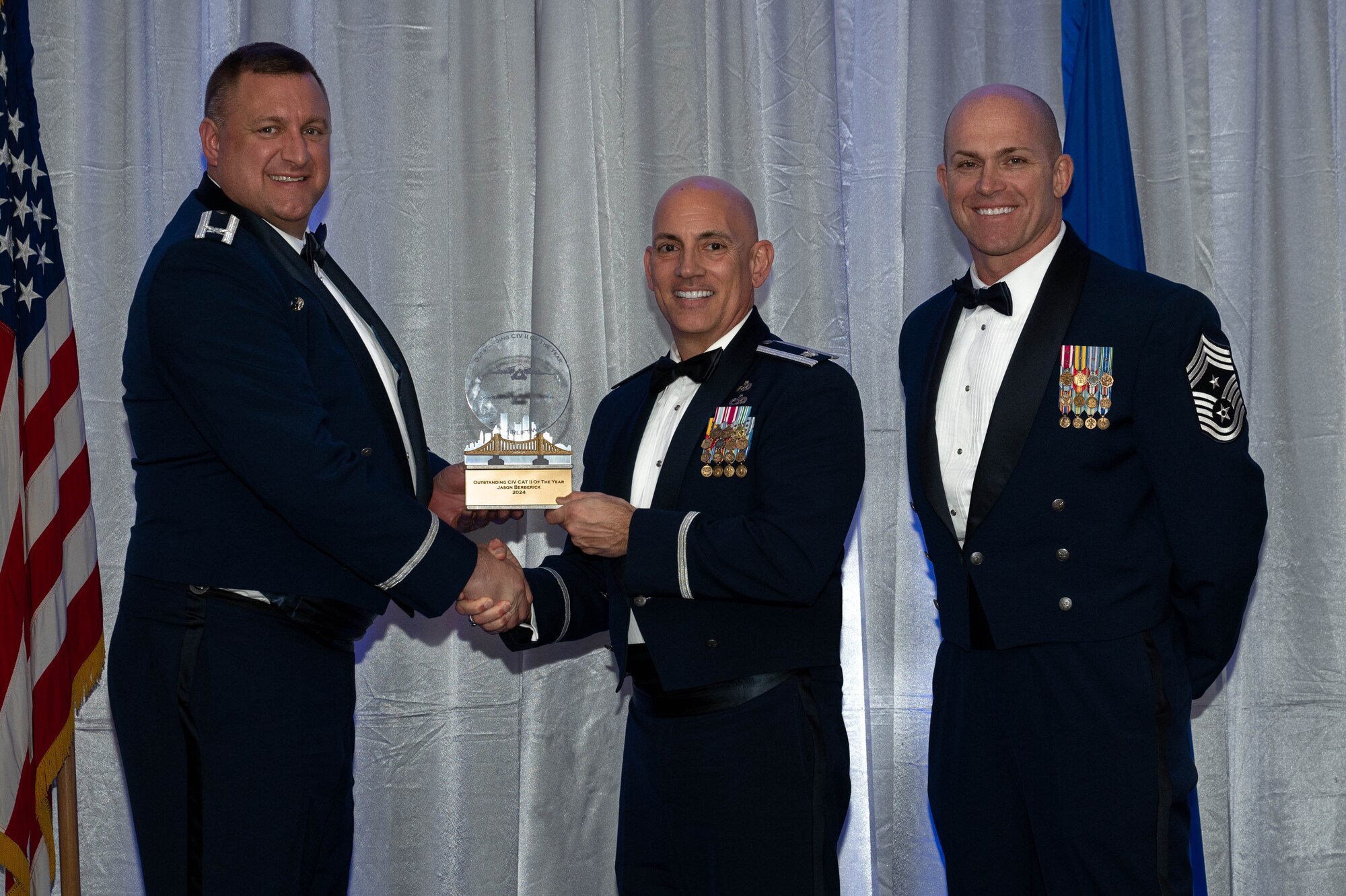 The commander and command chief hand over a trophy to an airmen during an awards banquet. All three are wearing blue suites called dress blues.