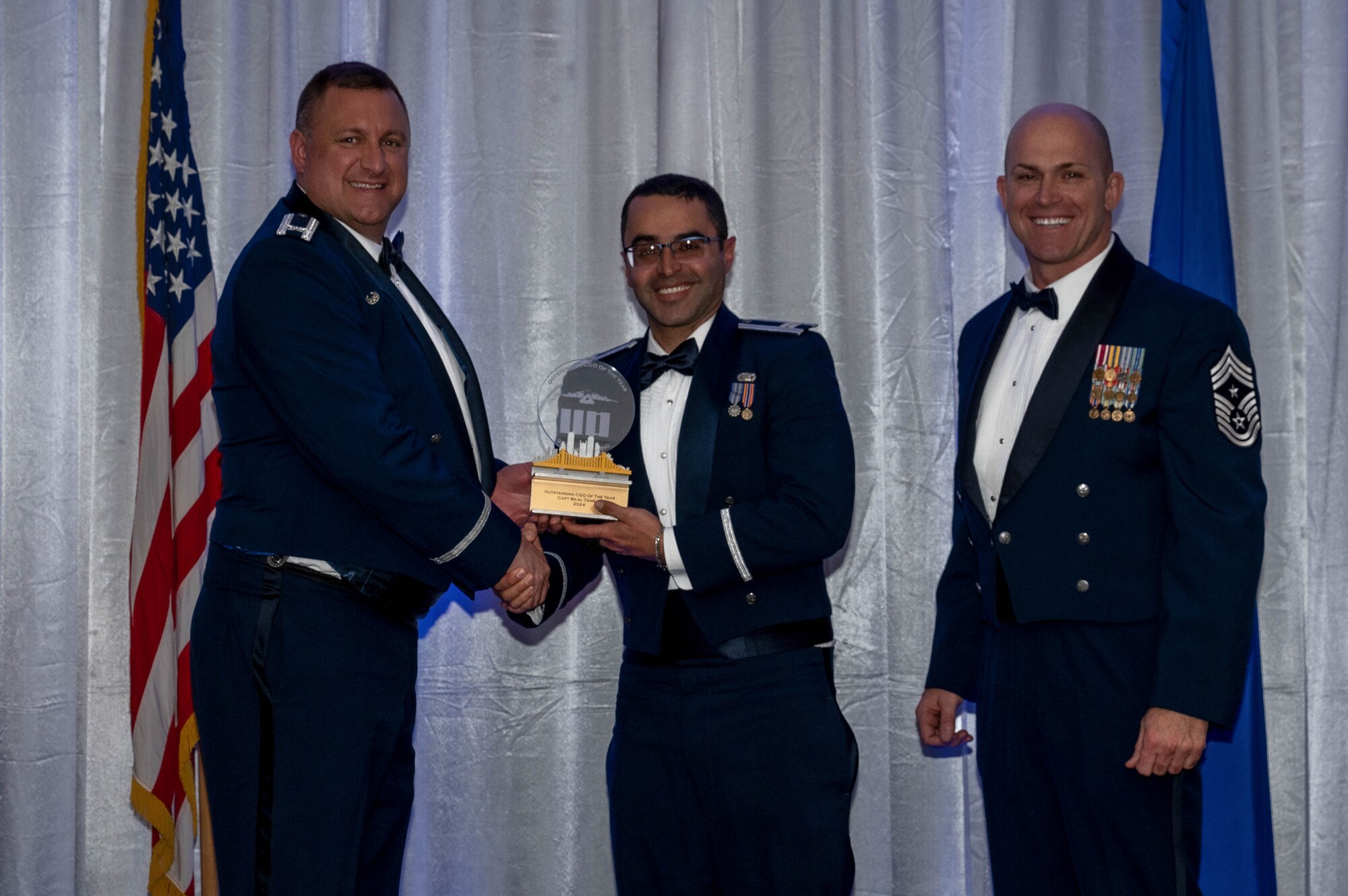The commander and command chief hand over a trophy to an airmen during an awards banquet. All three are wearing blue suites called dress blues.
