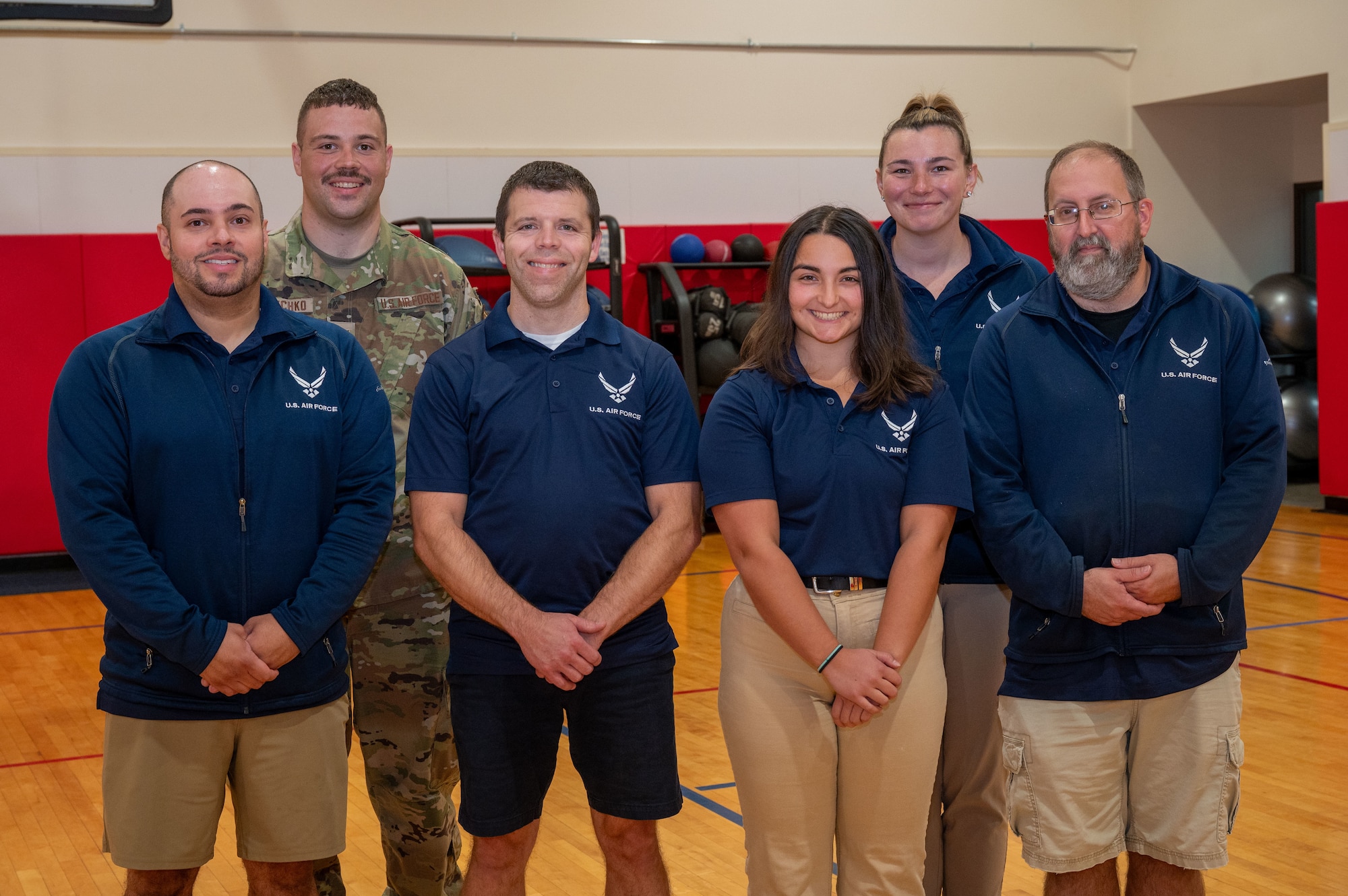 six people in wearing air force uniforms smile for a photo on a basket ball court. these people run the base's gym