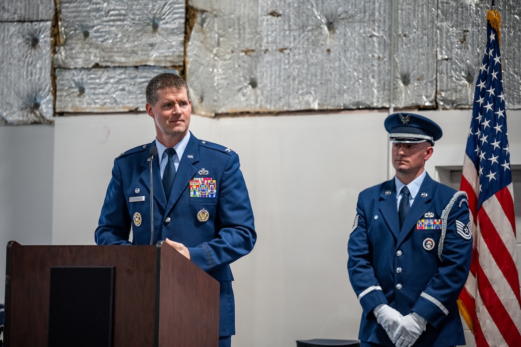 Col. Richards, in military service dress uniform, stands behind a podium and microphone