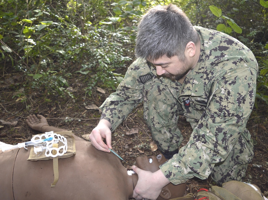 Making a practice point……Hospital Corpsman 2nd Class Yong Choe, assigned to Navy Medicine Readiness Training Command Bremerton hones his Tactical Combat Casualty Care abilities in an austere combat environment under the tutelage of Hospital Corpsman 1st Class (Fleet Marine Force qualified) Austin Santistevan, Urgent Care Clinic leading petty officer and course instructor. TCCC is an operational necessity for all corpsmen and is specifically designed to simulate the unique challenges and conditions on the field of battle in handling traumatic injuries. The week-long classroom and field training provided approximately 24 hospital corpsmen with knowledge-based instruction, followed by hands-on technique on how to provide emergency medical support and evacuation during a simulated combat environment. (Official Navy photo by Douglas H Stutz, NHB/NMRTC Bremerton public affairs officer)