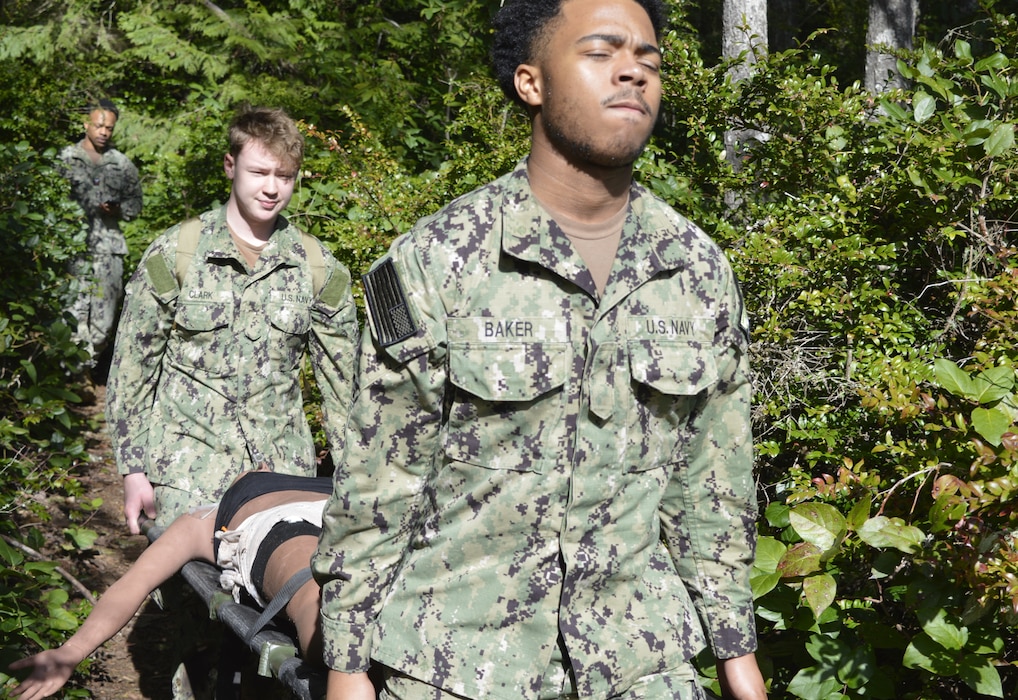Carrying the load ……Hospitalmen Tyree Baker and Joseph Clark, assigned to Navy Medicine Readiness Training Command Bremerton hones his Tactical Combat Casualty Care abilities in an austere combat environment under the tutelage of Hospital Corpsman 1st Class (Fleet Marine Force qualified) Austin Santistevan, Urgent Care Clinic leading petty officer and course instructor. TCCC is an operational necessity for all corpsmen and is specifically designed to simulate the unique challenges and conditions on the field of battle in handling traumatic injuries. The week-long classroom and field training provided approximately 24 hospital corpsmen with knowledge-based instruction, followed by hands-on technique on how to provide emergency medical support and evacuation during a simulated combat environment. (Official Navy photo by Douglas H Stutz, NHB/NMRTC Bremerton public affairs officer)