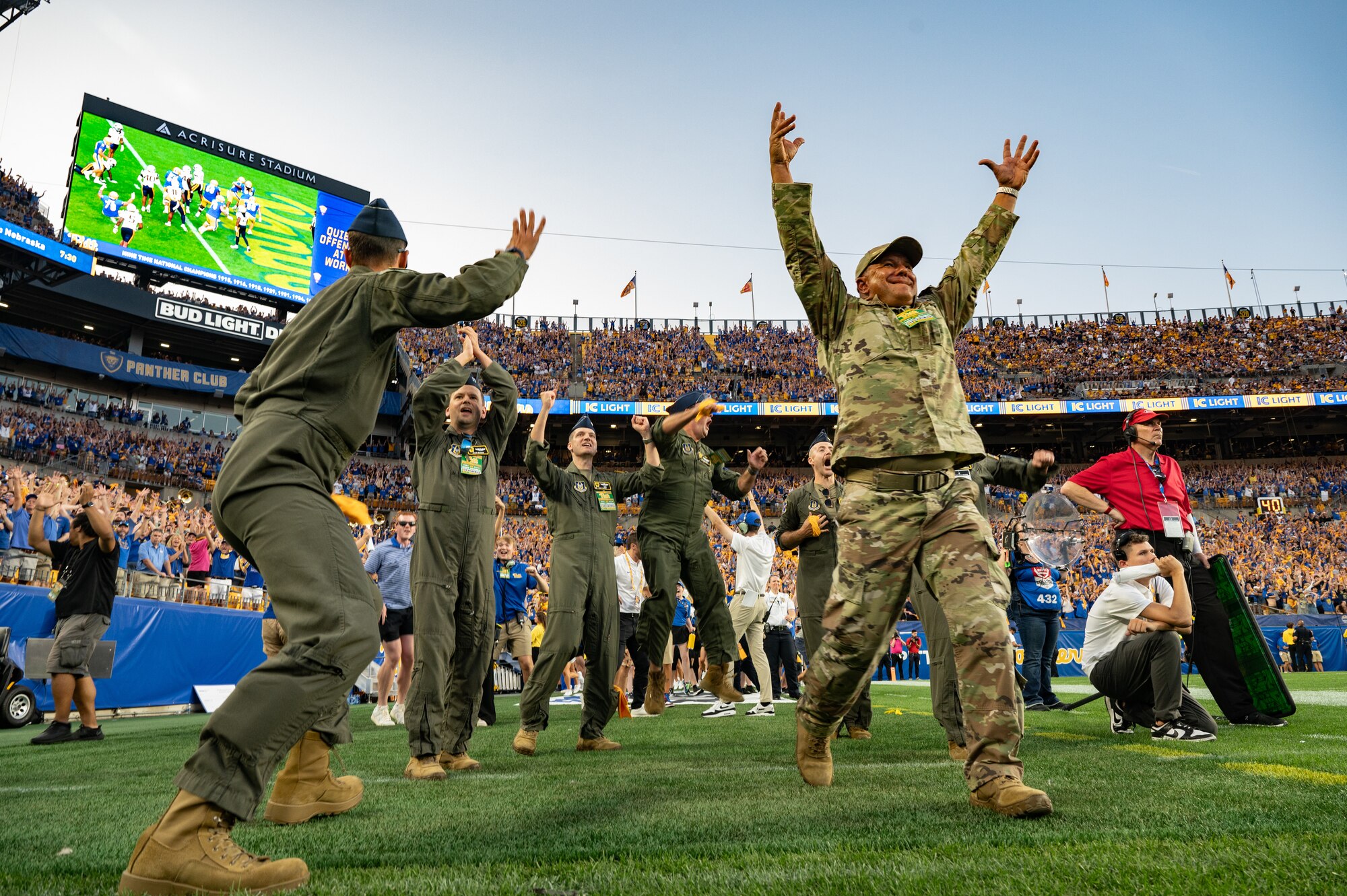 Airmen in military uniforms celebrate on the field of Acrisure stadium during a football game