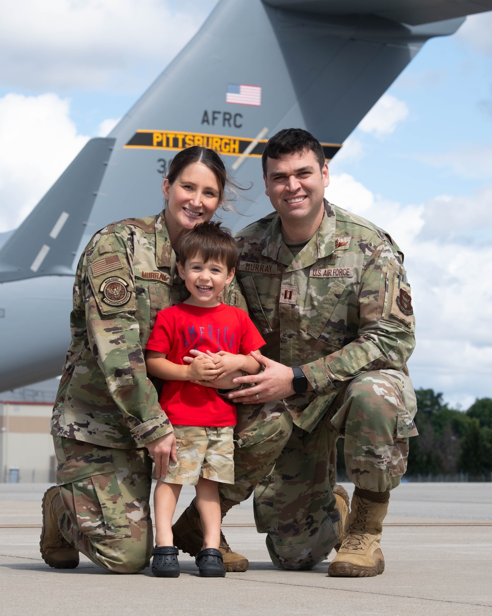 a mother and father wearing a military uniform embrace their son next to a c-17 globemaster III
