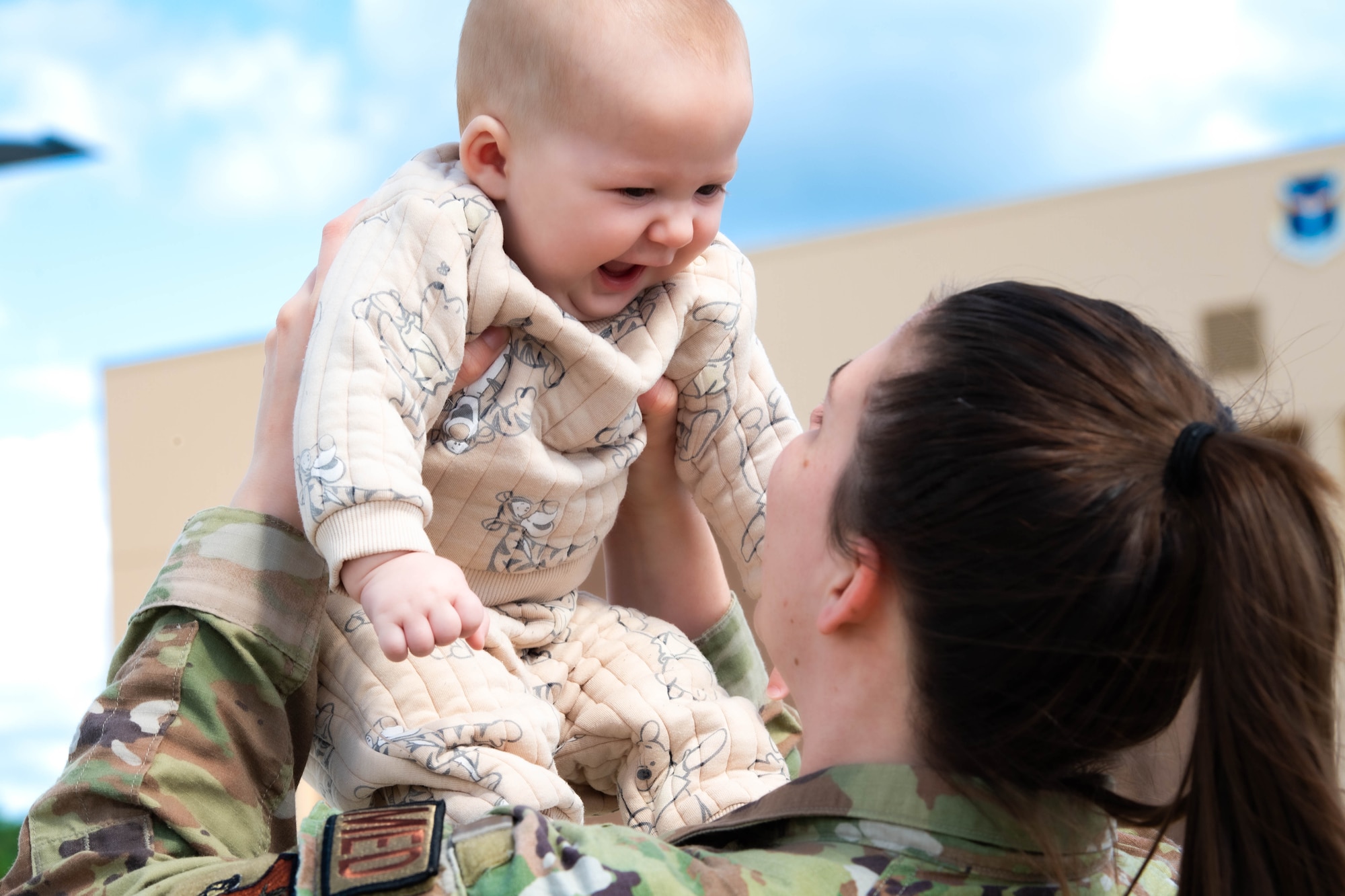 a mother wearing a military uniform hold up her child  next to a c-17 globemaster III