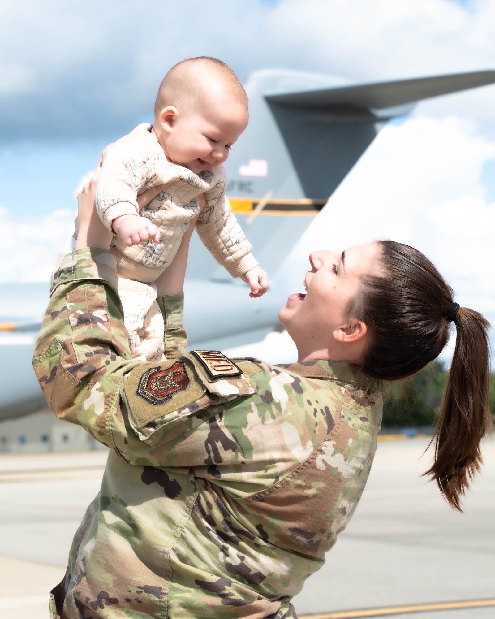 a mother wearing a military uniform hold up her child  next to a c-17 globemaster III