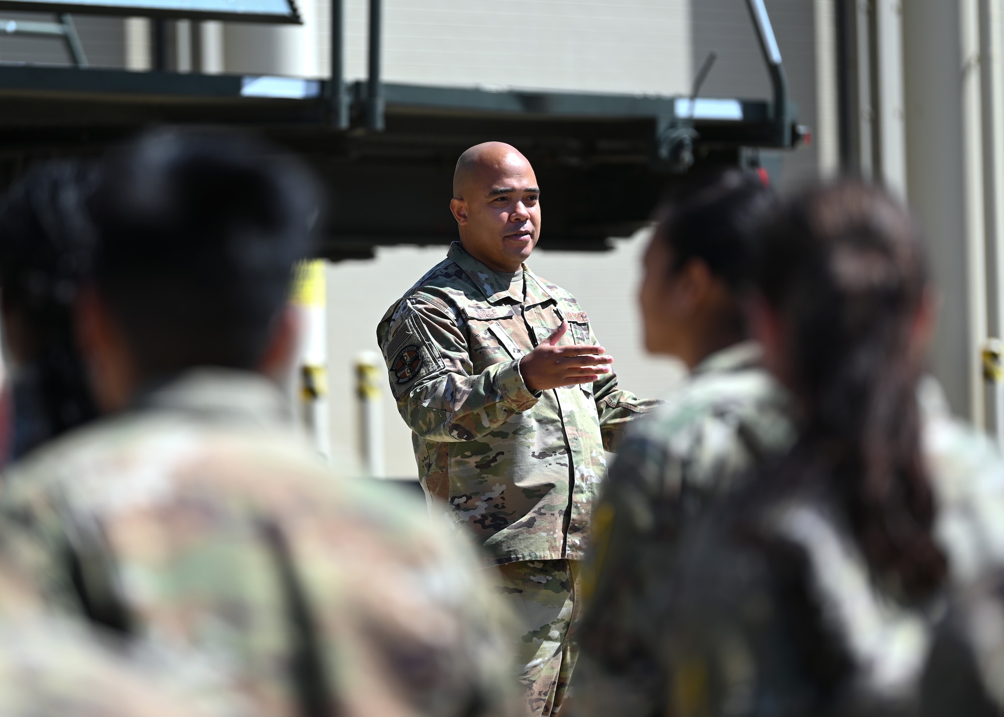 a military members speaks to a group of airmen outside of LRS maintenance building during a promotion ceremony, sun shining