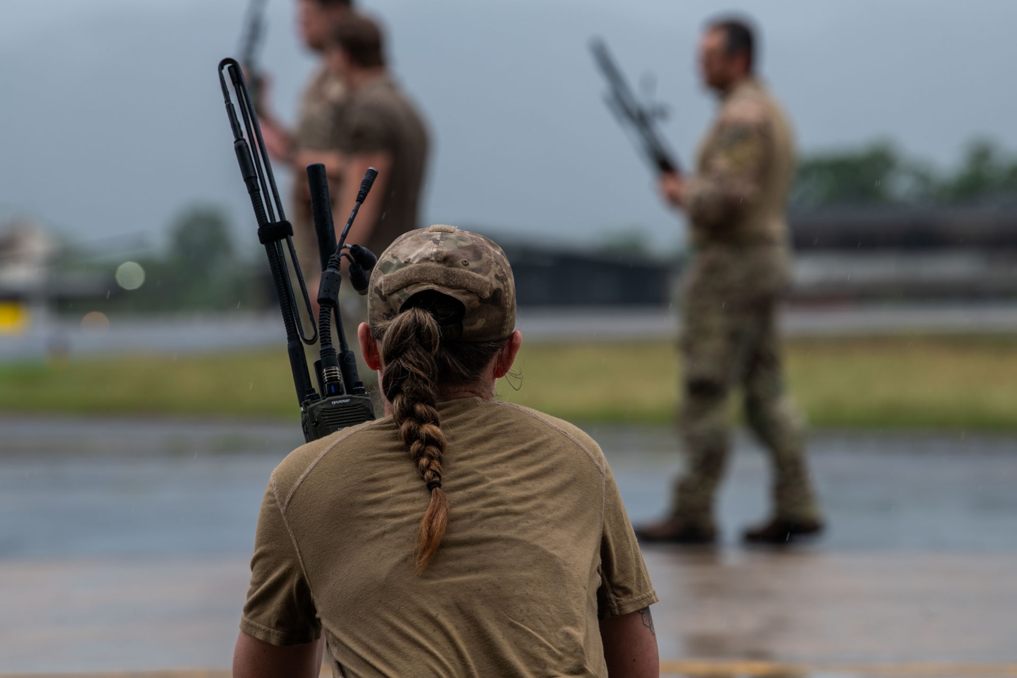 An Airman listens to a handheld radio with their back to the camera