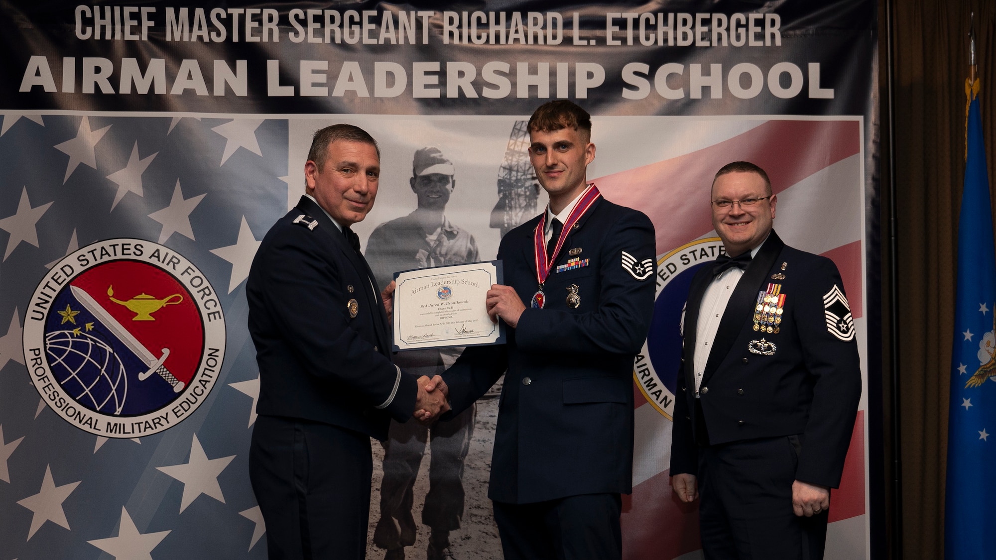 Col. Reynaldo Champion, commander of the 319th Mission Support Group and Chief Master Sgt. Aaron Smith, 319th Medical Group Senior Enlisted Leader present Staff Sgt. Jared W. Bronikowski, assigned to the 319th Security Forces Squadron with an Airman Leadership School graduation certificate at Grand Forks Air Force Base, N.D., May 8, 2025. (U.S. Air Force photo by Airman Nailah Pacheco)