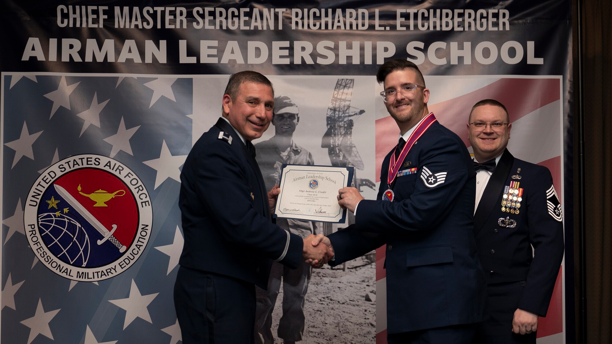 Col. Reynaldo Champion, commander of the 319th Mission Support Group and Chief Master Sgt. Aaron Smith, 319th Medical Group Senior Enlisted Leader present Staff Sgt. Andrew L. Cradit, assigned to the 319th Operations Support Squadron with an Airman Leadership School graduation certificate at Grand Forks Air Force Base, N.D., May 8, 2025. (U.S. Air Force photo by Airman Nailah Pacheco)