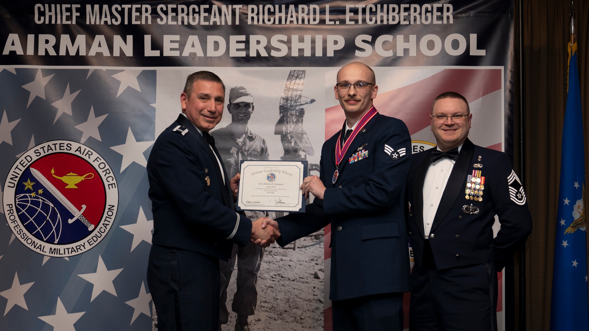 Col. Reynaldo Champion, commander of the 319th Mission Support Group and Chief Master Sgt. Aaron Smith, 319th Medical Group Senior Enlisted Leader present Senior Airman Dillon D. Gorsma, assigned to the 319th Operations Support Squadron with an Airman Leadership School graduation certificate at Grand Forks Air Force Base, N.D., May 8, 2025. (U.S. Air Force photo by Airman Nailah Pacheco)