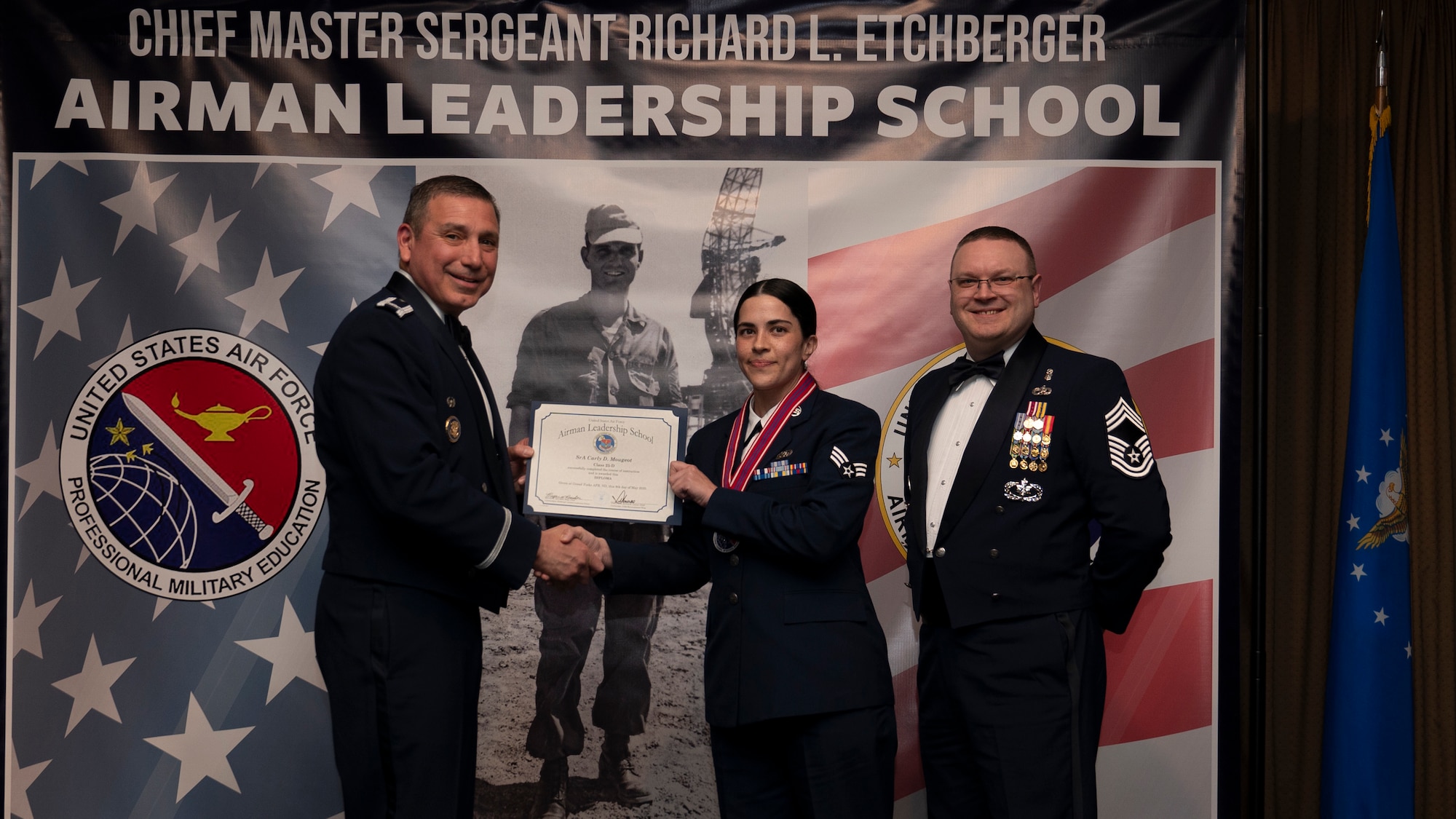 Col. Reynaldo Champion, commander of the 319th Mission Support Group and Chief Master Sgt. Aaron Smith, 319th Medical Group Senior Enlisted Leader present Senior Airman Carly D. Mougeot, assigned to the 319th Communications Squadron with an Airman Leadership School graduation certificate at Grand Forks Air Force Base, N.D., May 8, 2025. (U.S. Air Force photo by Airman Nailah Pacheco)