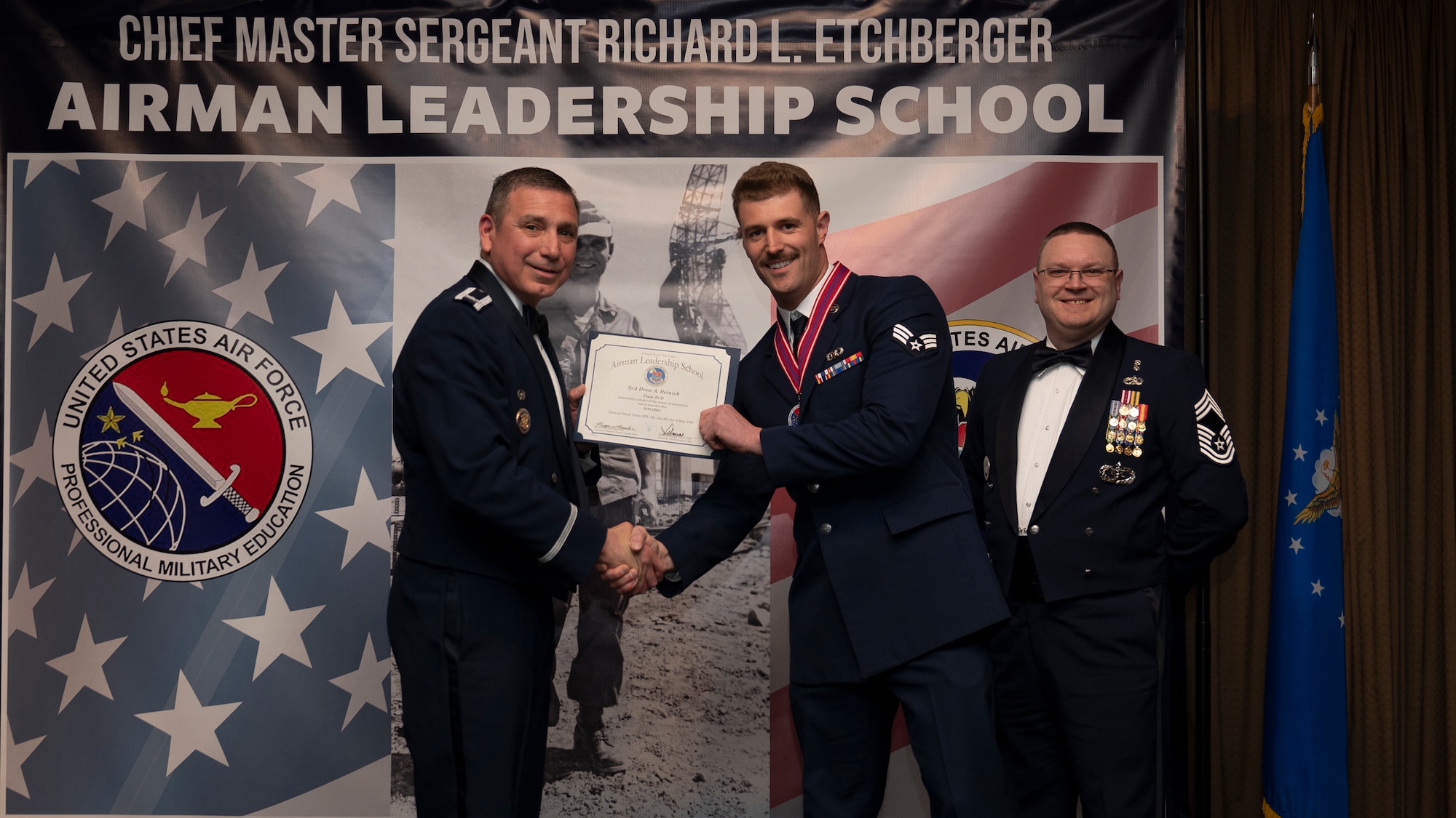 Col. Reynaldo Champion, commander of the 319th Mission Support Group and Chief Master Sgt. Aaron Smith, 319th Medical Group Senior Enlisted Leader present Senior Airman Drew A. Reinick, assigned to the 128th Operations Support Squadron with an Airman Leadership School graduation certificate at Grand Forks Air Force Base, N.D., May 8, 2025. (U.S. Air Force photo by Airman Nailah Pacheco)