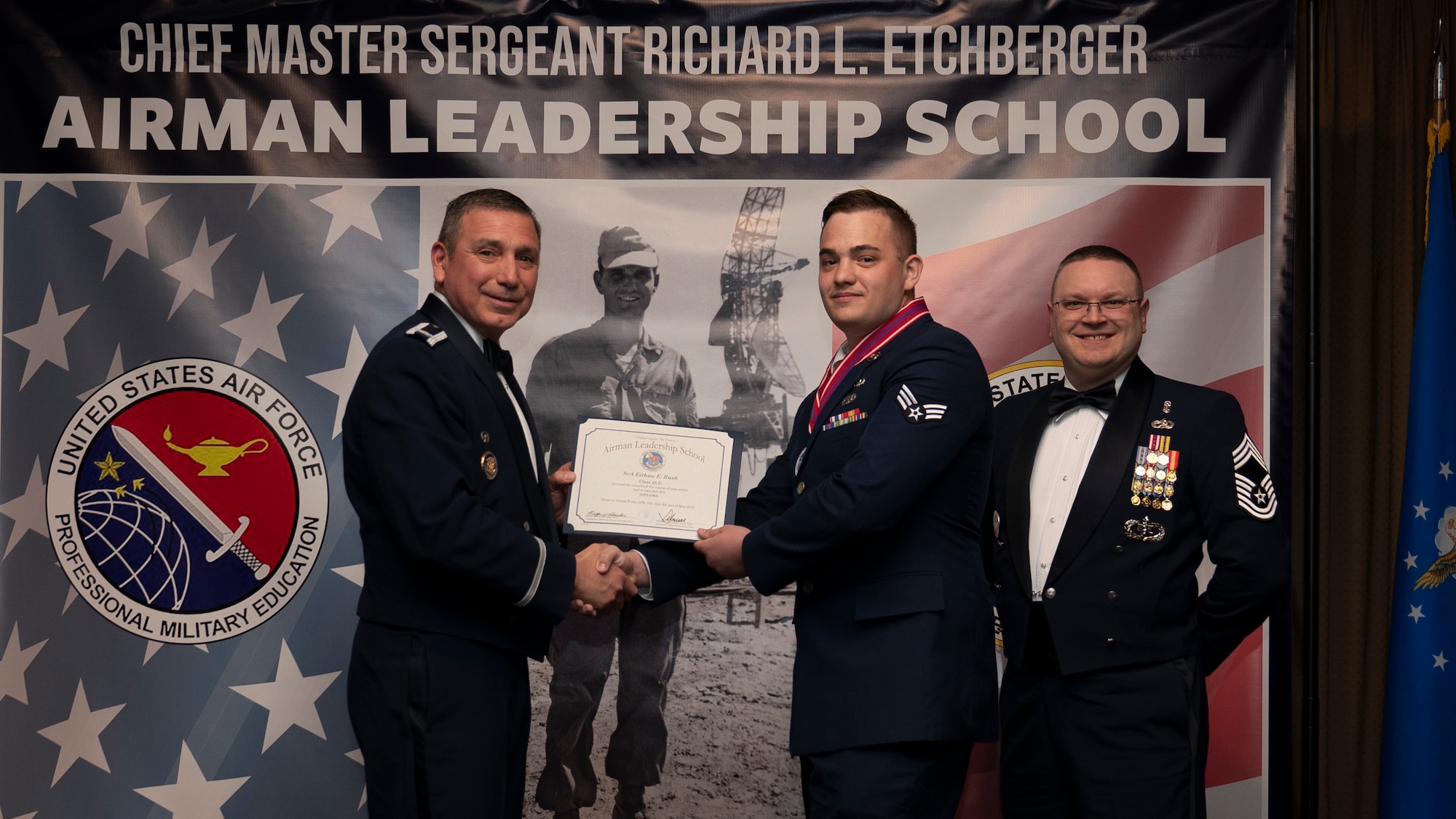 Col. Reynaldo Champion, commander of the 319th Mission Support Group and Chief Master Sgt. Aaron Smith, 319th Medical Group Senior Enlisted Leader present Senior Airman Eithan E. Rush, assigned to the 142nd Maintenance Squadron with an Airman Leadership School graduation certificate at Grand Forks Air Force Base, N.D., May 8, 2025. (U.S. Air Force photo by Airman Nailah Pacheco)