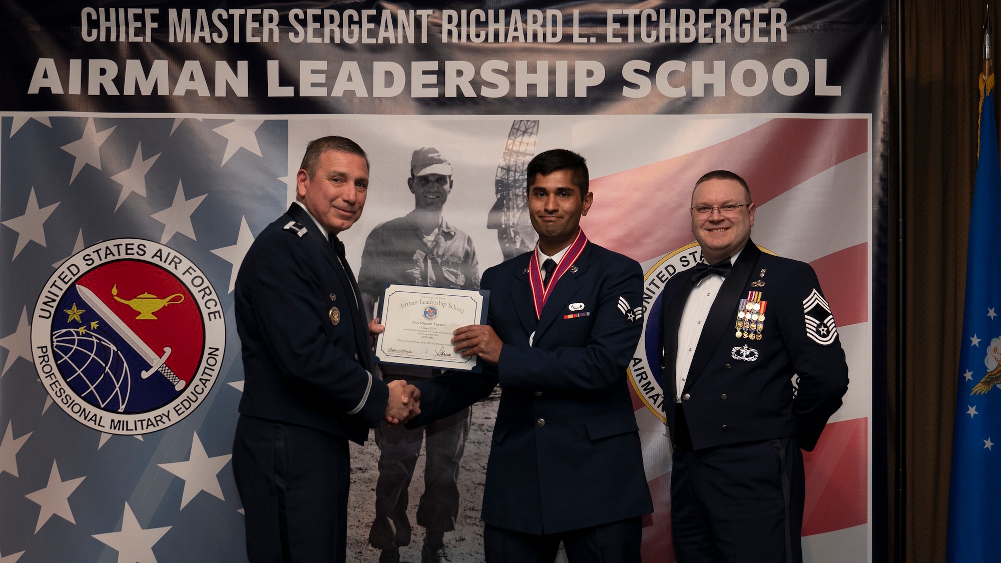 Col. Reynaldo Champion, commander of the 319th Mission Support Group and Chief Master Sgt. Aaron Smith, 319th Medical Group Senior Enlisted Leader present Senior Airman Dipesh Tiwari, assigned to the 319th Force Support Squadron with an Airman Leadership School graduation certificate at Grand Forks Air Force Base, N.D., May 8, 2025. (U.S. Air Force photo by Airman Nailah Pacheco)