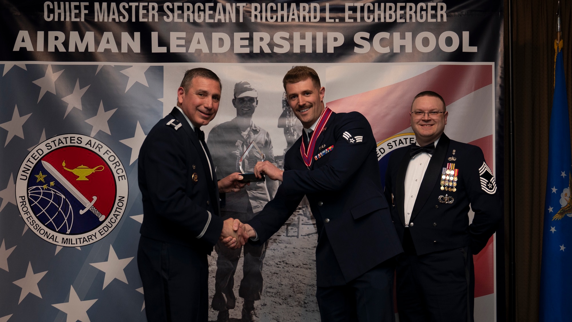 Col. Reynaldo Champion, commander of the 319th Mission Support Group and Chief Master Sgt. Aaron Smith, 319th Medical Group Senior Enlisted Leader present Senior Airman Drew A. Reinick, assigned to the 128th Operations Support Squadron with the Academic Achievement Award at Grand Forks Air Force Base, N.D., May 8, 2025. (U.S. Air Force photo by Airman Nailah Pacheco)