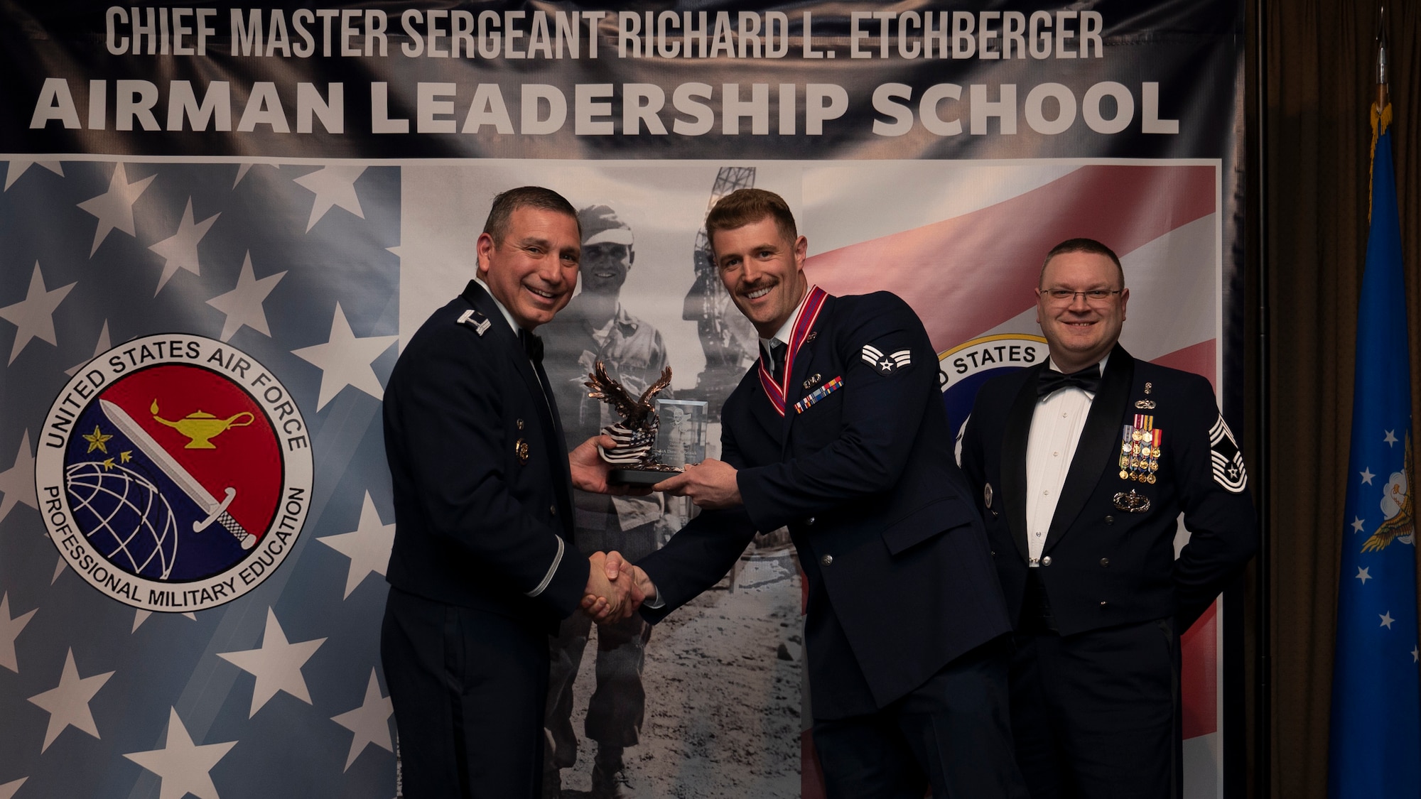 Col. Reynaldo Champion, commander of the 319th Mission Support Group and Chief Master Sgt. Aaron Smith, 319th Medical Group Senior Enlisted Leader present Senior Airman Drew A. Reinick, assigned to the 128th Operations Support Squadron with the Academic Achievement Award at Grand Forks Air Force Base, N.D., May 8, 2025. (U.S. Air Force photo by Airman Nailah Pacheco)