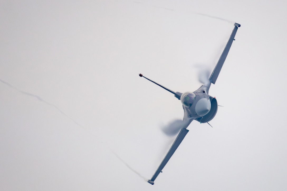 A flying jet, with wings tilted; the contrail is visible behind the aircraft.